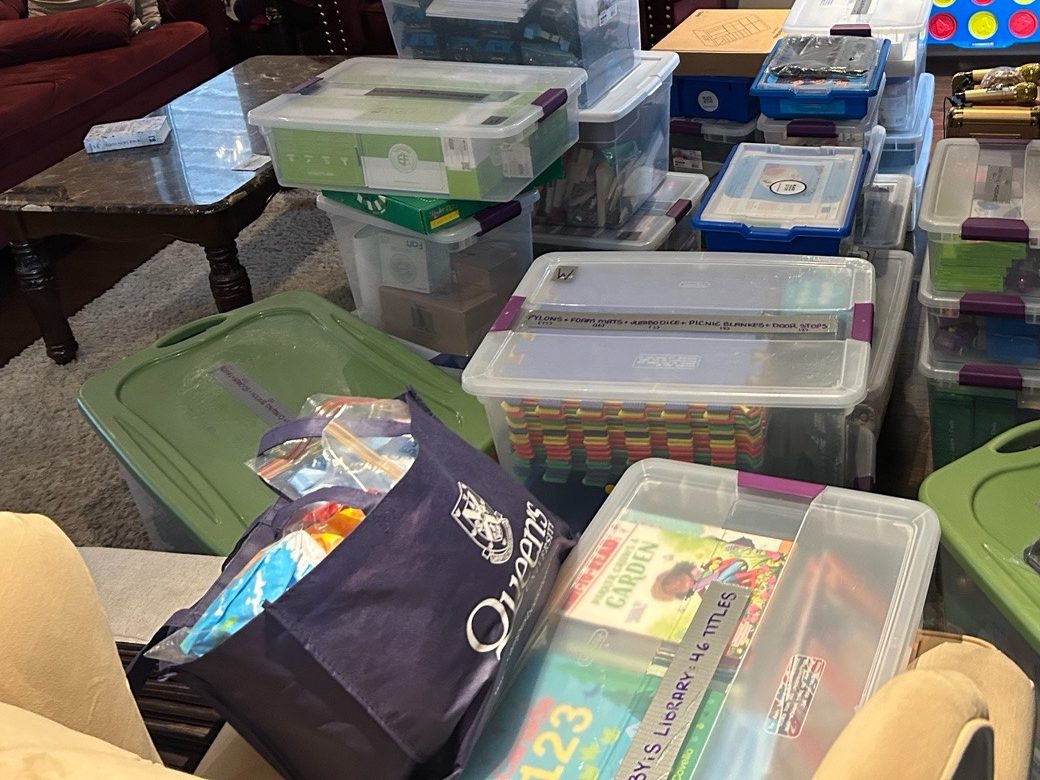 Bins of donated STEM equipment and books, beside a Queen's University tote bag.